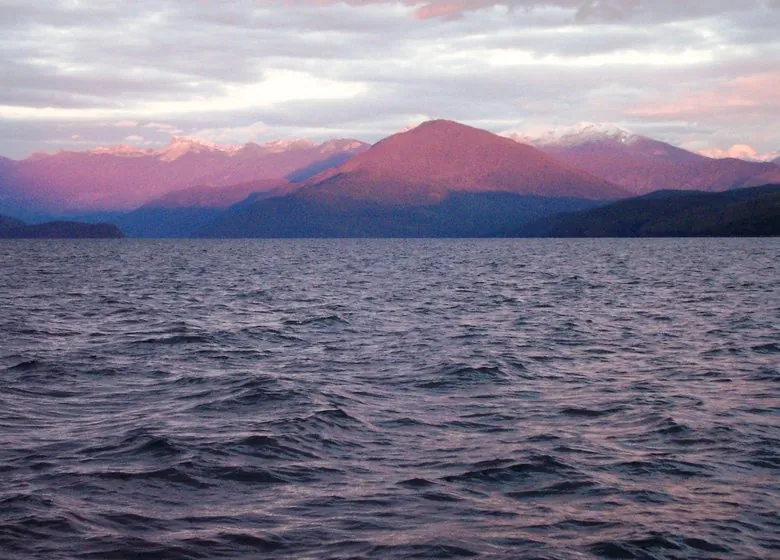 Quesnel Lake at sunset, the far peaks lit pink above wind-rippled water
