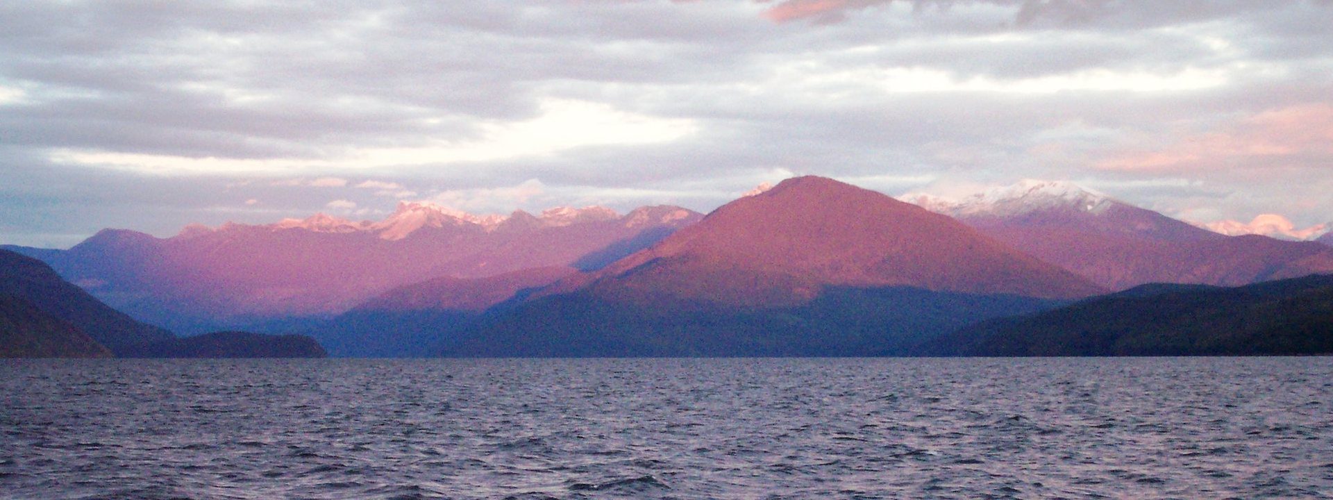 Quesnel Lake at sunset, the far peaks lit pink above wind-rippled water