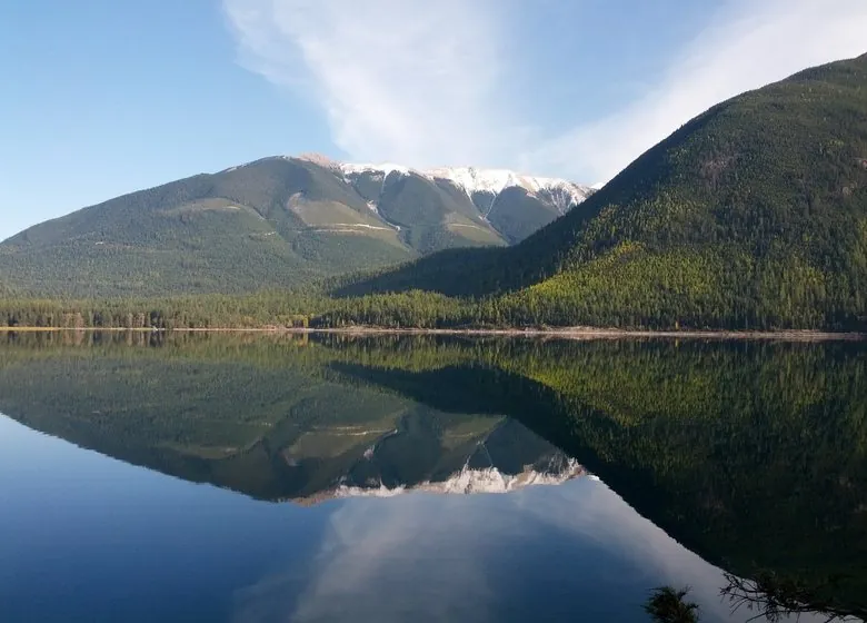 Whiteswan Lake at dawn, forested mountains and a snowy ridge reflected in calm water