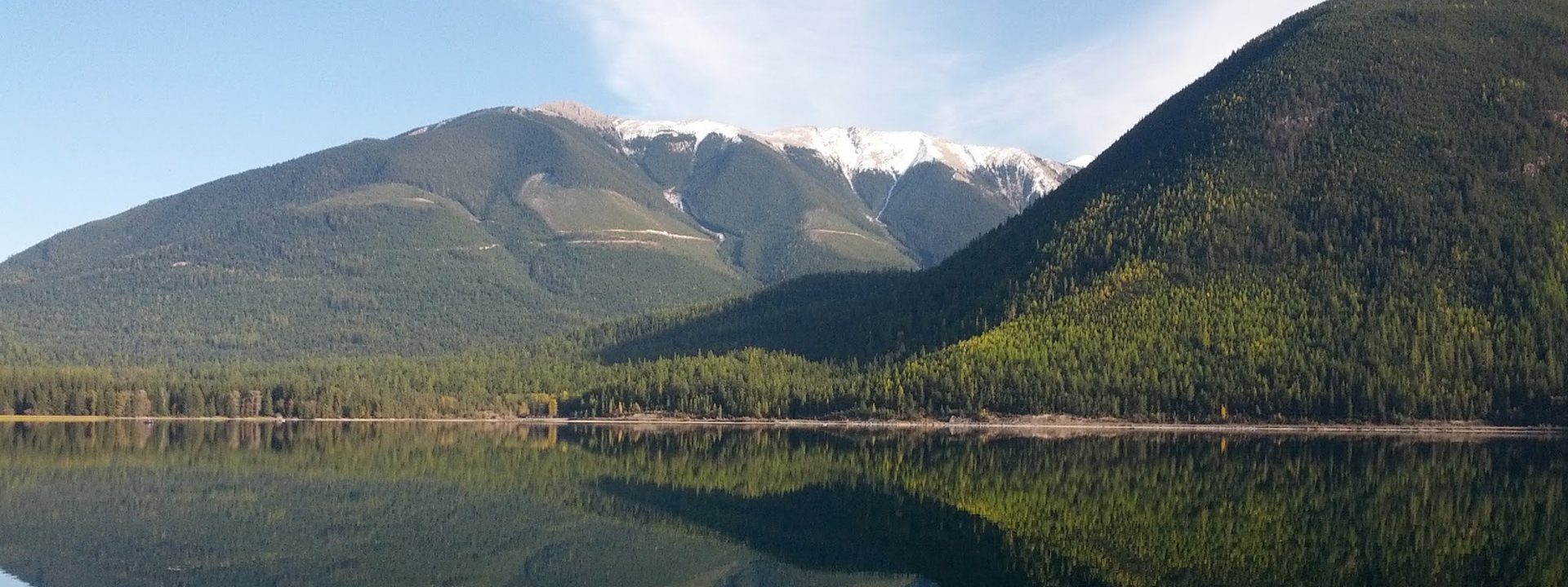 Whiteswan Lake at dawn, forested mountains and a snowy ridge reflected in calm water