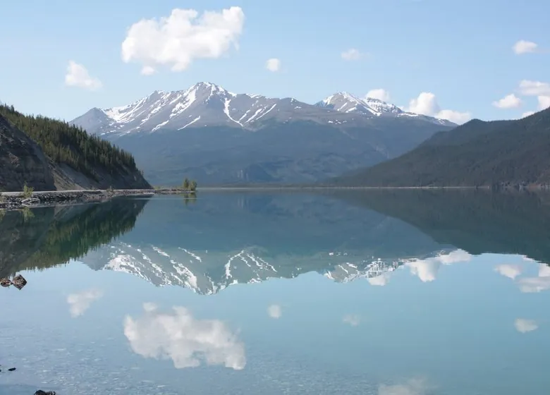 Muncho Lake, jade water mirroring snow-streaked mountains and white clouds