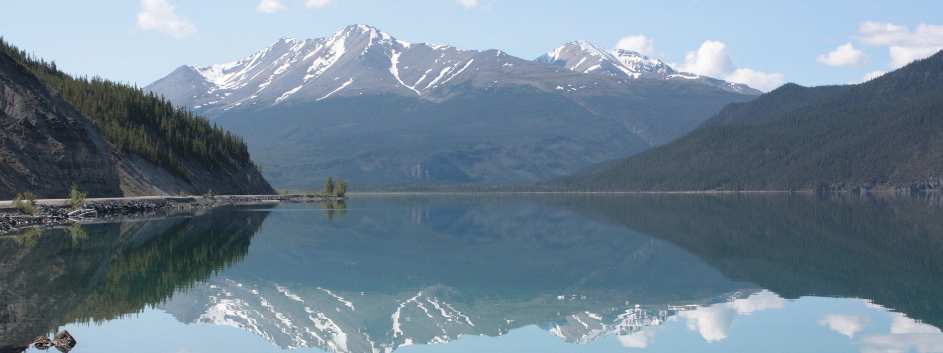Muncho Lake, jade water mirroring snow-streaked mountains and white clouds
