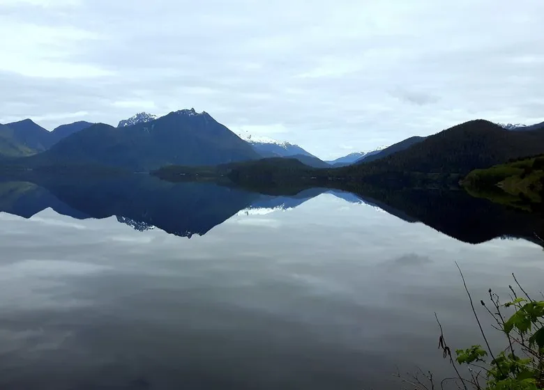 Kennedy Lake on a still, overcast day, the mountains mirrored in the water