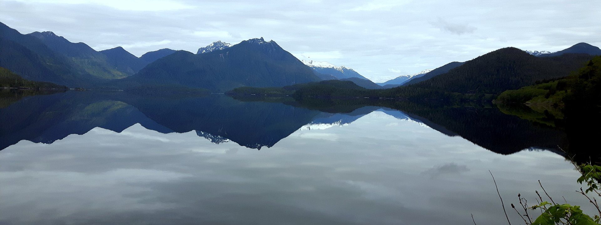 Kennedy Lake on a still, overcast day, the mountains mirrored in the water